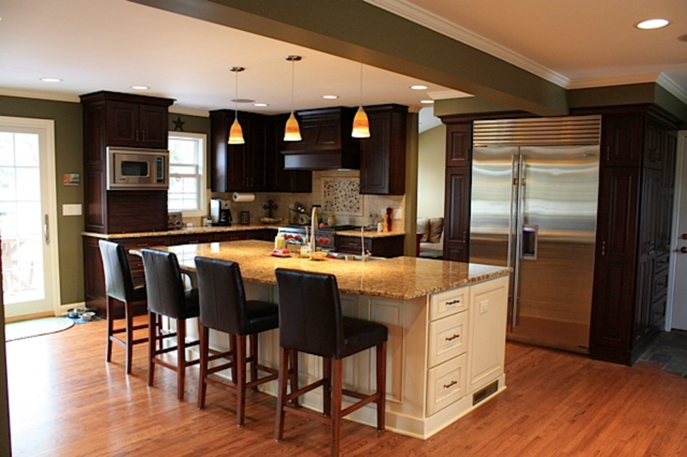 Modern kitchen with dark wood cabinetry, granite countertop, and stainless steel appliances, featuring bar seating and natural light from a nearby door.