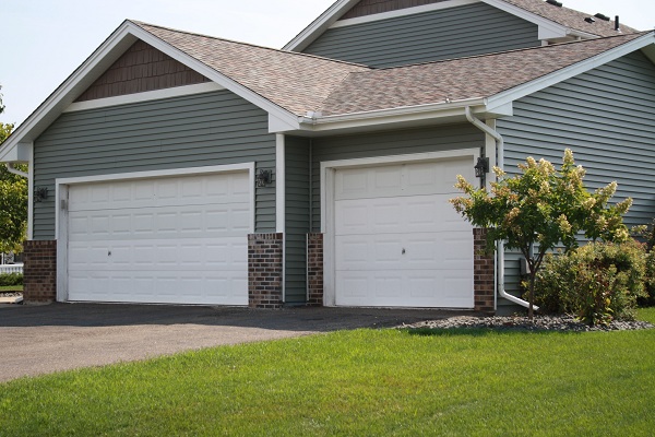 Residential garage with modern design, featuring two white garage doors, gray siding, brick accents, and well-maintained green lawn, emphasizing durability and curb appeal for Minnesota homes.