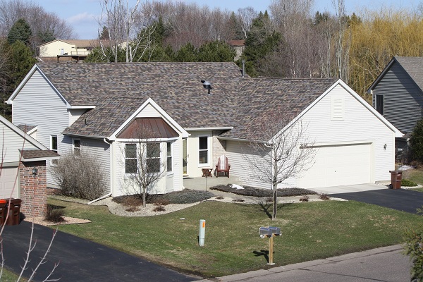 Residential home with a durable, stylish roof featuring a mix of textures and colors, showcasing storm resilience and curb appeal, surrounded by landscaped yard in Oakdale, MN.