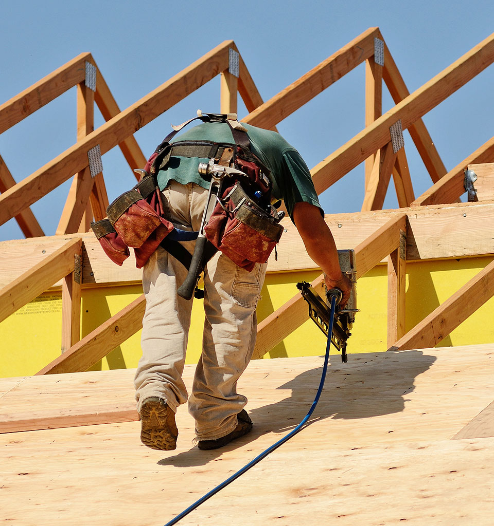 Construction worker using a nail gun on a wooden roof structure, showcasing expertise in roofing and home improvement services.