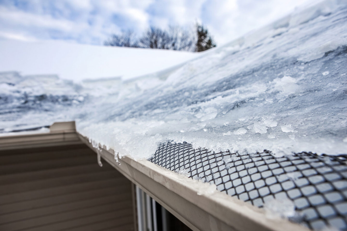 Ice accumulation on a roof's edge with a gutter guard, highlighting winter weather challenges and ice dam prevention for Twin Cities homes.